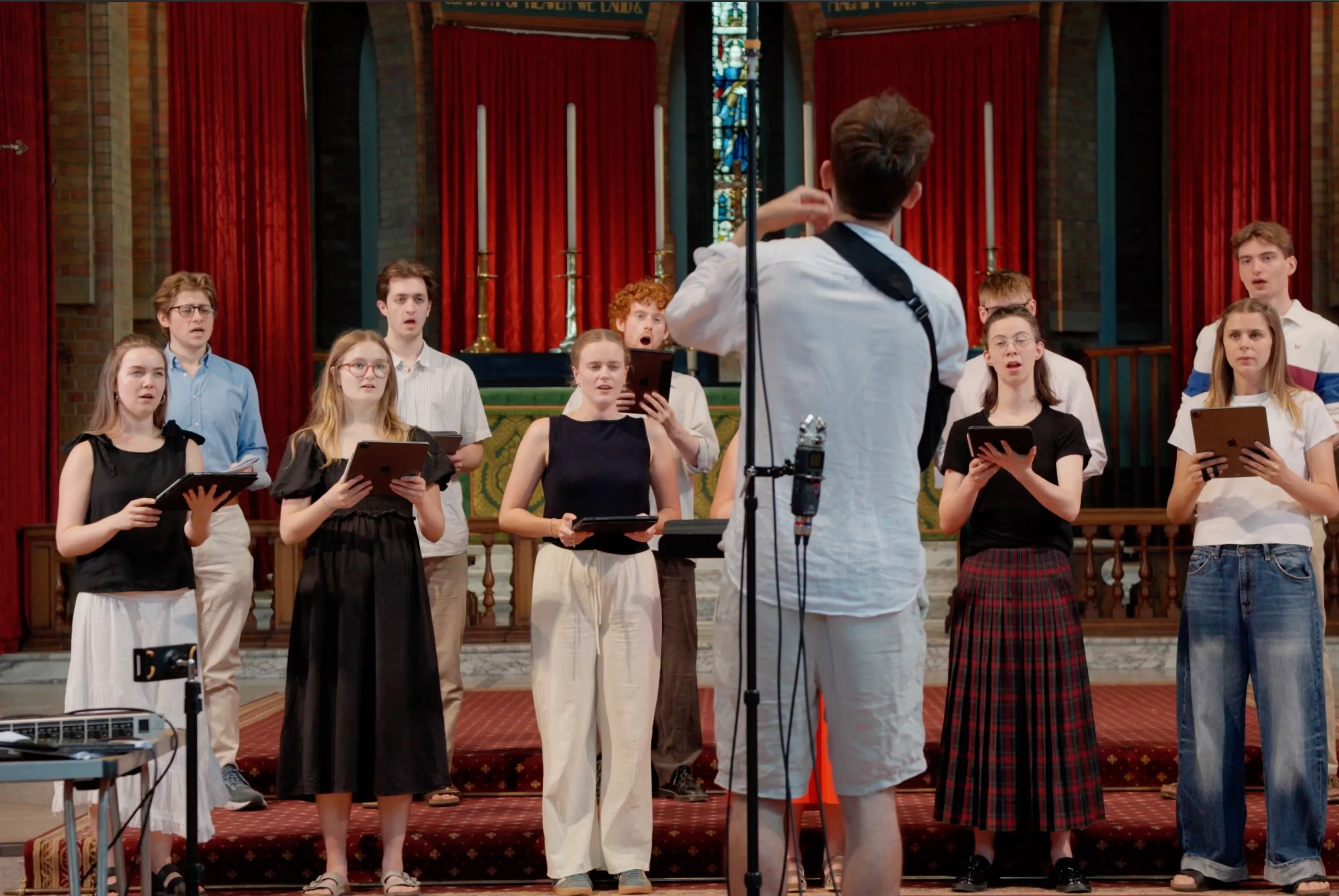 The full Alma Consort choir performing to a conductor, with recording microphones set up in a London church.